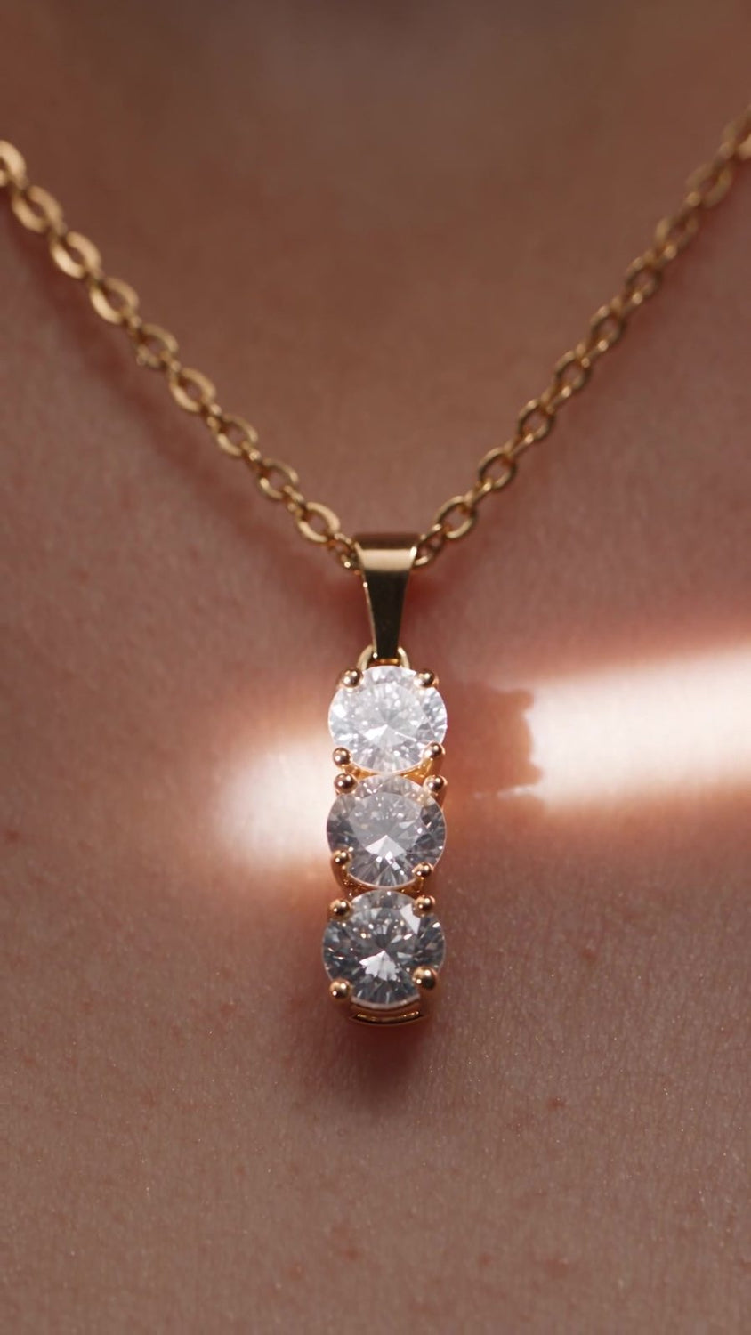 Cascade worn at the collarbone, with a band of warm light across the skin